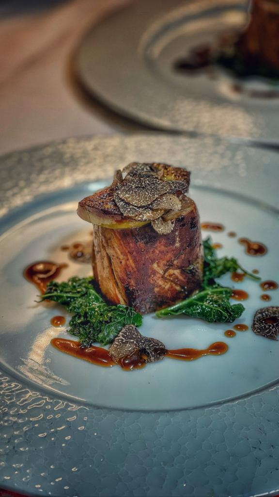 Plated Black Angus beef tenderloin topped with pan-seared foie gras and black truffle slices, served with crispy kale and beef jus.